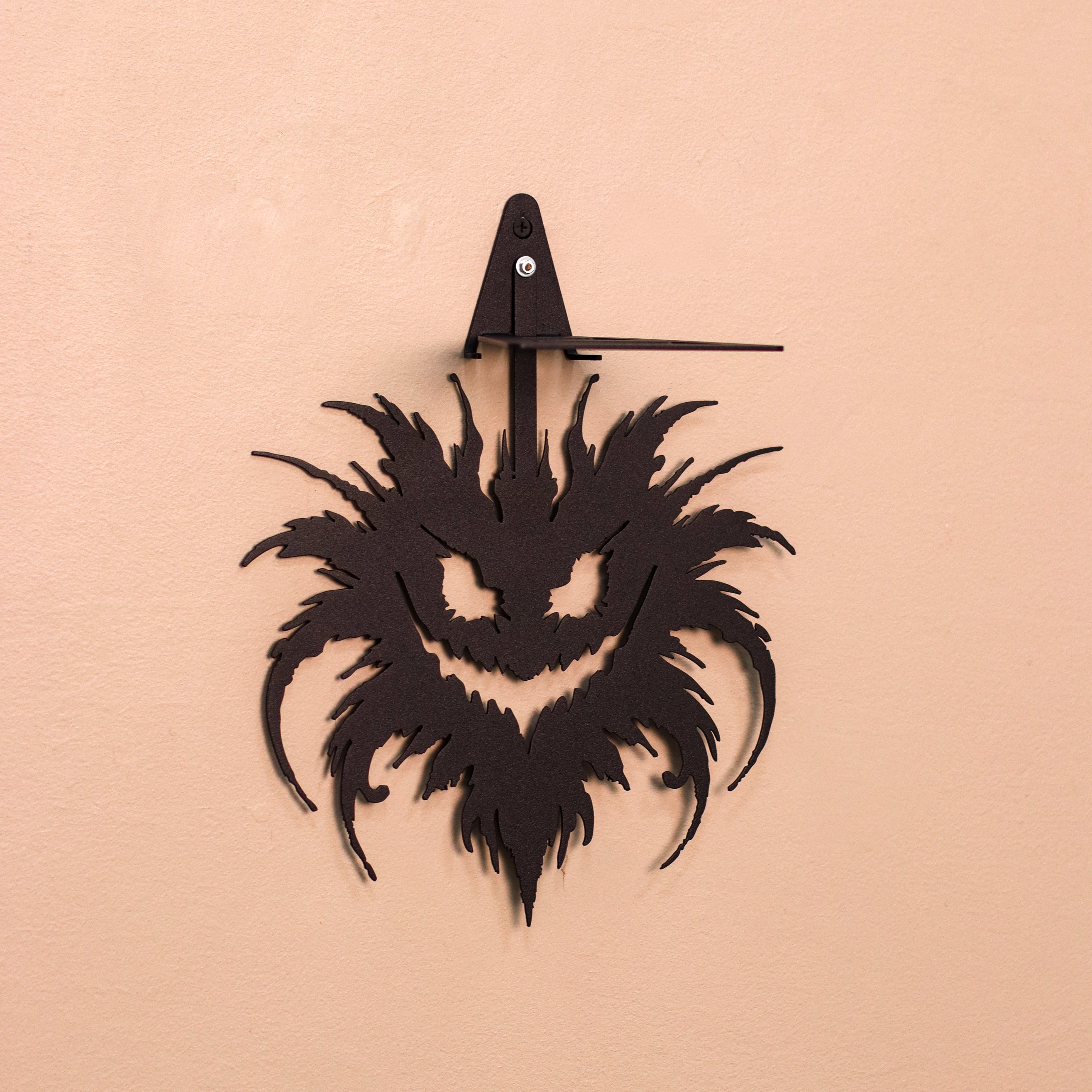 A black metal wall clock shaped like a stylized monster face with sharp, spiky hair, mounted on a textured peach-colored wall.