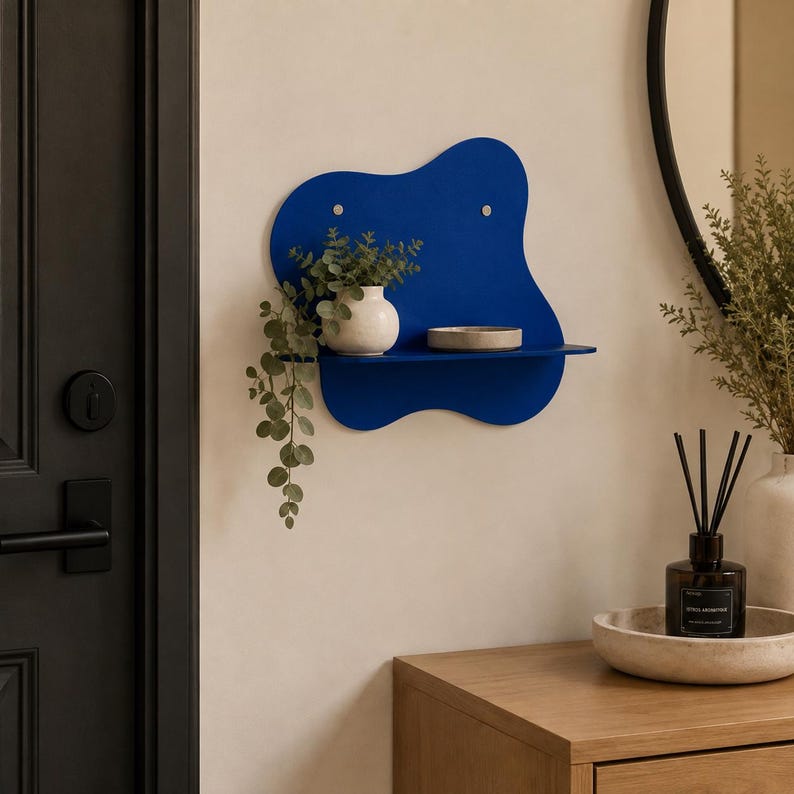 Abstract metal floating wall shelf with wavy back panel displaying a small vase and decorative dish