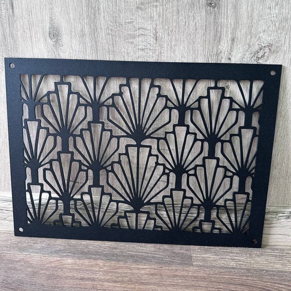 A rectangular black metal decorative panel with an Art Deco fan pattern, displayed against a rustic wood plank background.