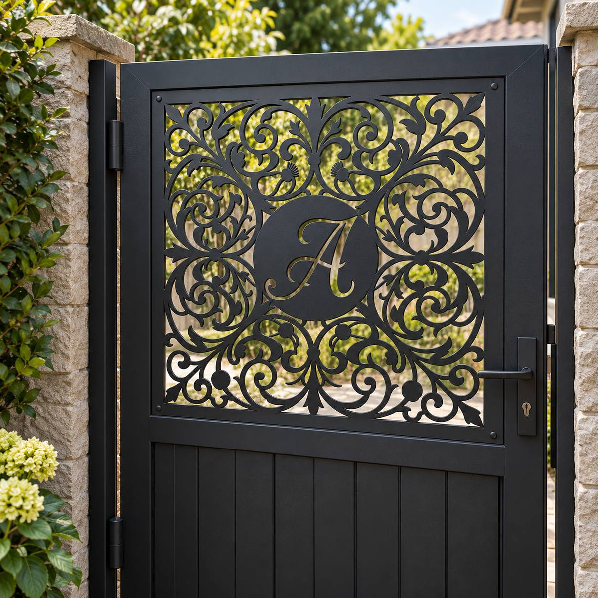 A black metal gate with an ornate scrollwork design and a central circular monogram letter 'A', set between stone pillars with green foliage in the background.
