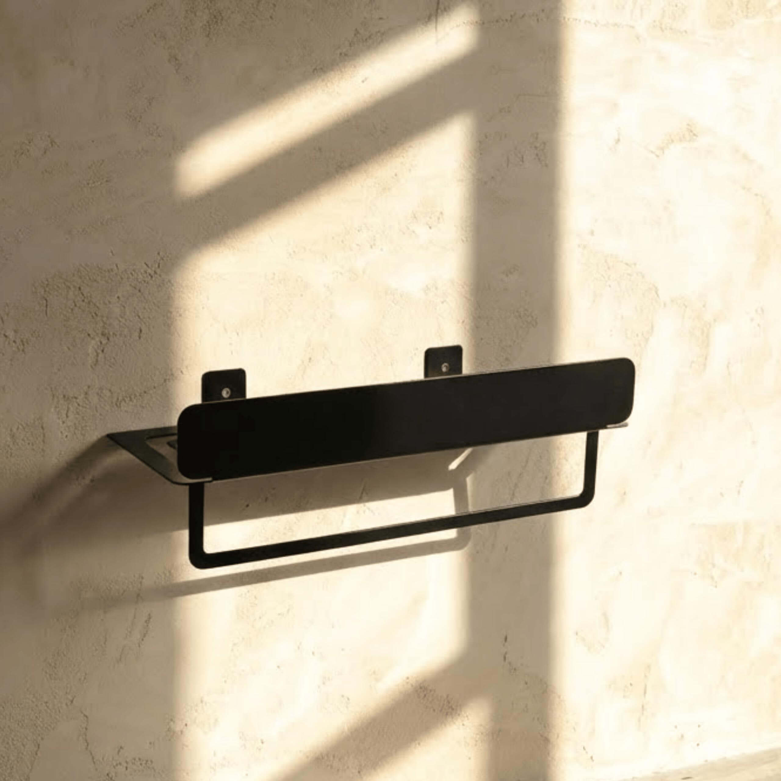 Black towel rack mounted on a textured wall with soft shadows
