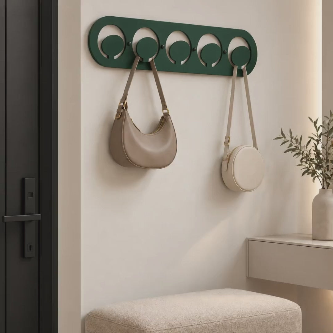 Dark green metal wall hook rack with circular hooks holding handbags in a modern entryway